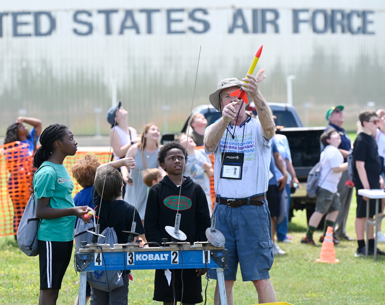 A volunteer instructor holds a model rocket while explaining the launch process to a group of students during Aerospace Camp at the National Museum of the U.S. Air Force. The students watch closely, gathered around the instructor outdoors on the museum grounds.