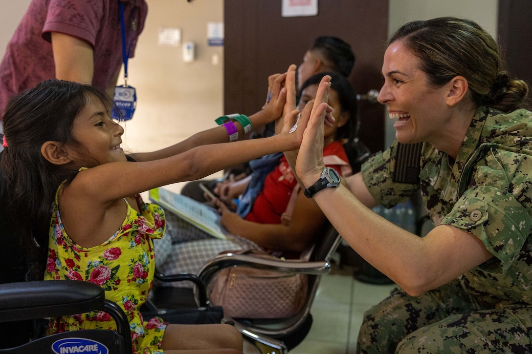 A sailor high-fives a smiling child in a room with three other people.