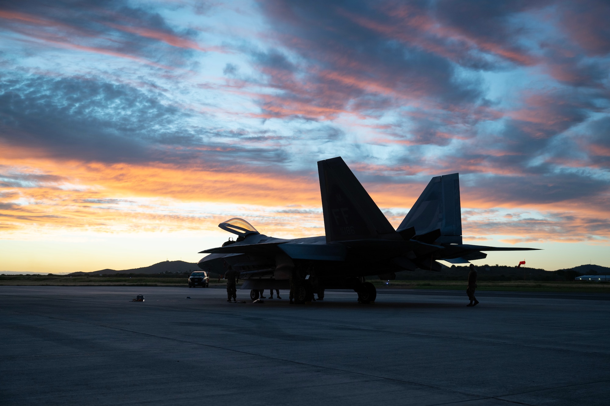 F-22 on flightline during sunset with Airmen performing maintenance