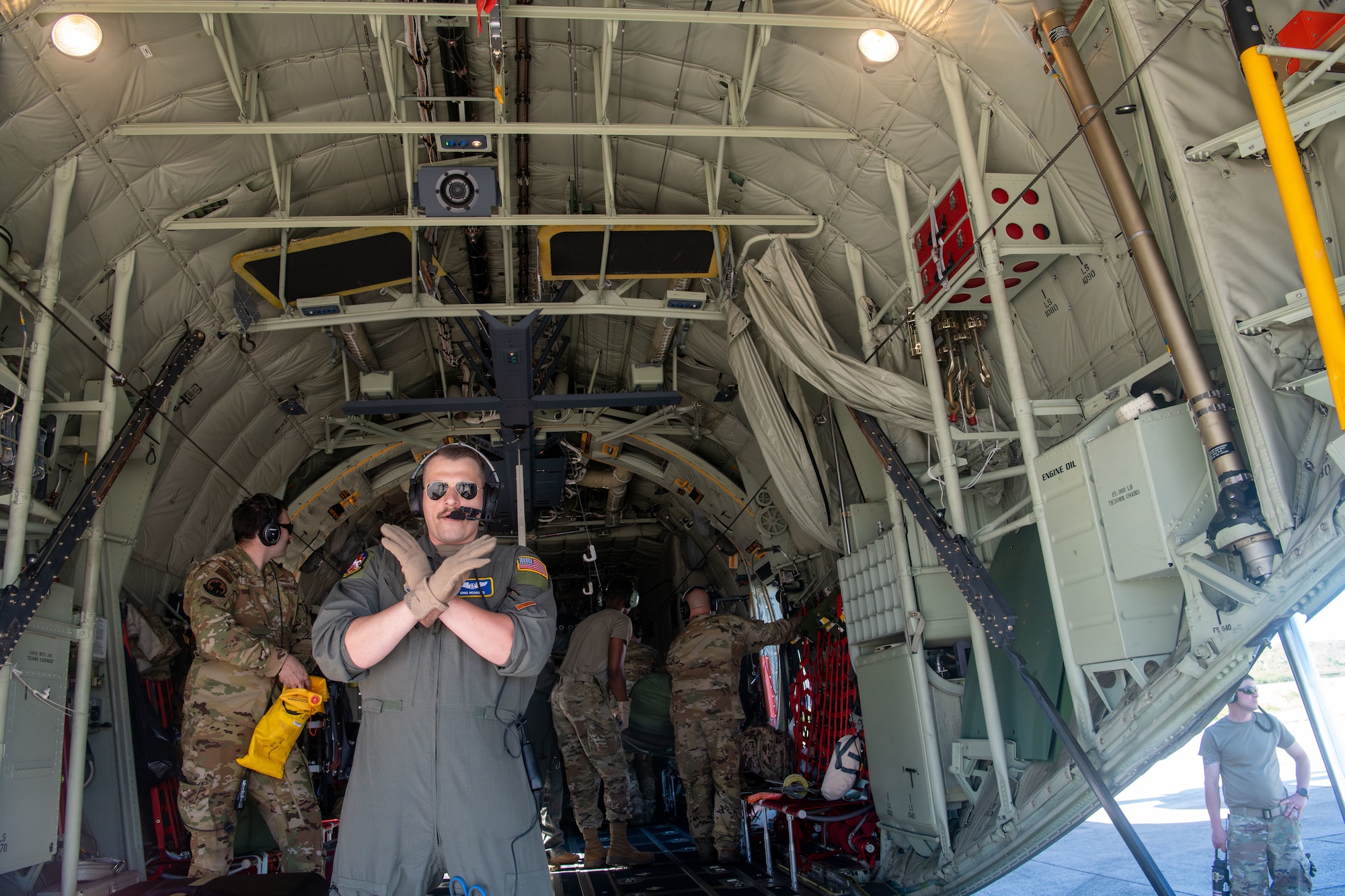 Airman holds arms in an X pattern on the ramp of a C-130J Hercules aircraft
