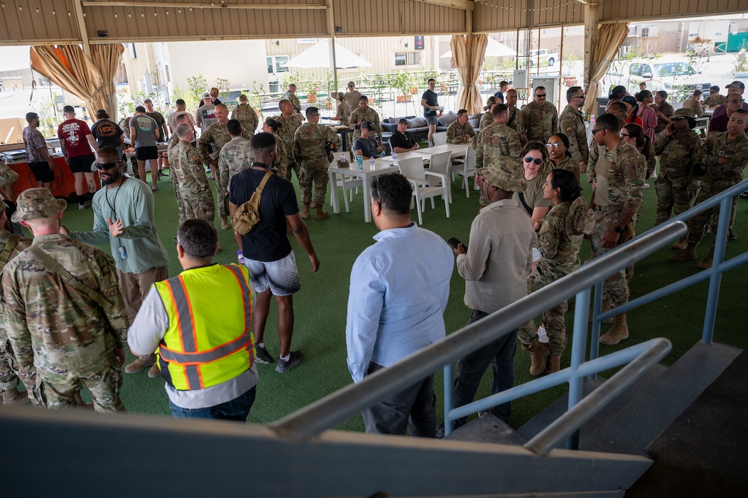 A group of Airmen are grouped and huddled under an overhang awaiting barbecue serving