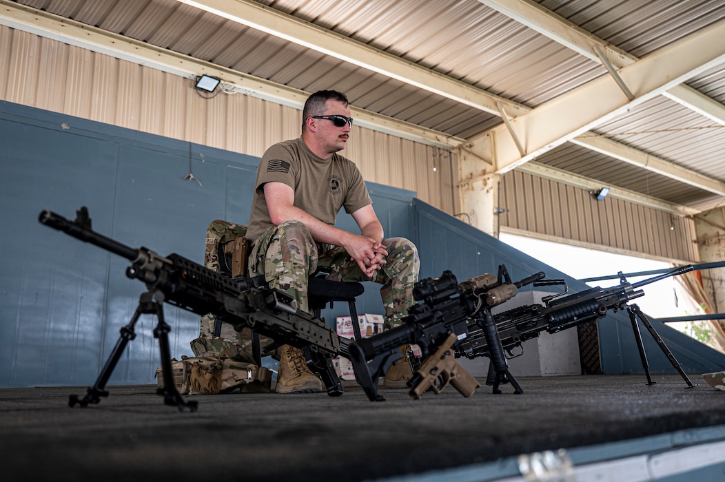 Tech. Sgt. Jacob Thayer sits on stage with a variety of machine guns displayed in front of him for Airmen and other guests to see them in a showcase