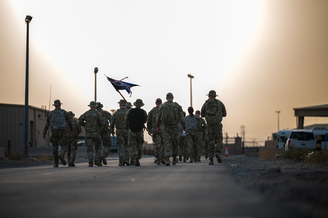 A group of Airmen walk away from the camera as silhouettes casted against the bright white of the sun in the sky