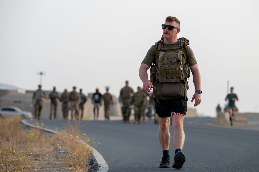 Senior Airman Dustin Whiten walks toward camera in the foreground with a group of Airmen in the background out of focus
