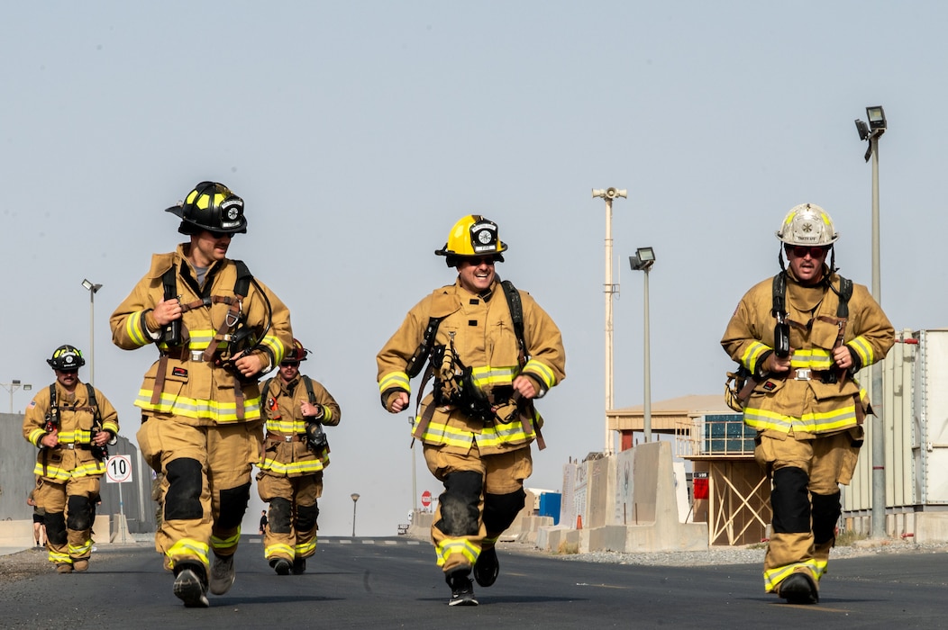A group of five firefighters, three in front, two in back, run toward the camera during a ruck march