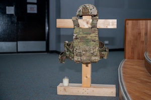 An armor stand holding a vest and helmet with a candle at its base sits mid-frame in low-light