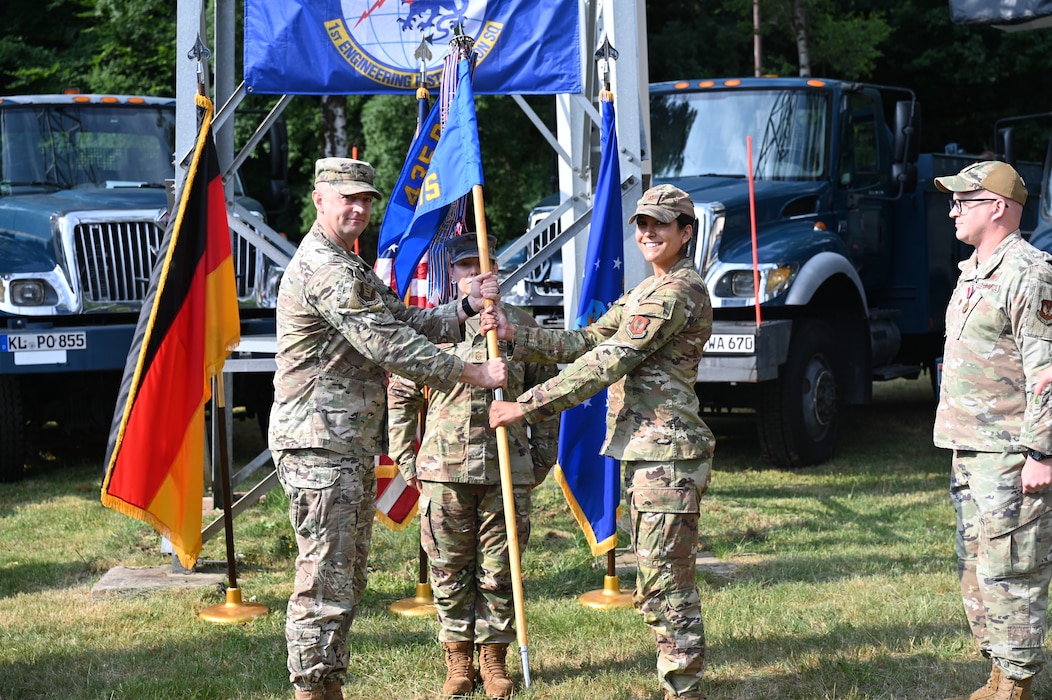 KAPAUN AIR STATION, Germany -- Col. Scott A. Weed, 435th Communications Operations Group commander (Left) passes the guidon to Maj. Lesly M. Torres, during the 1st Engineering Installation Squadron change of command at Kapaun Air Station, July 3, 2025. The ceremony highlighted the departure of Maj. Caleb E. Mays and the accomplishments of the squadron during his leadership while also outlining Torres’s capabilities in leading the squadron. (U.S Air Force photo by Capt. Lou Burton)
