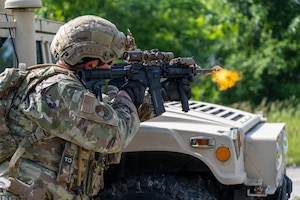 Airman fires simulated rounds. Military vehicle in the forground.