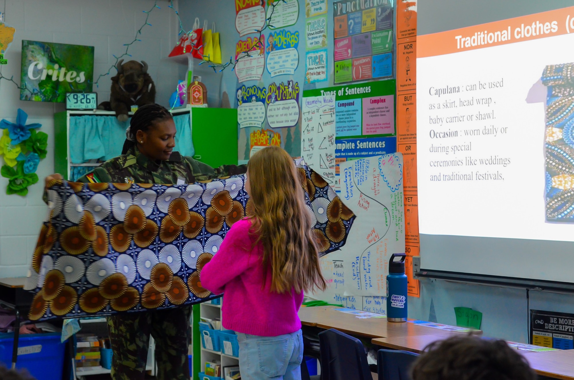 A Defense Language Institute English Language Center student shows an elementary school student a capulana, a traditional clothing item.