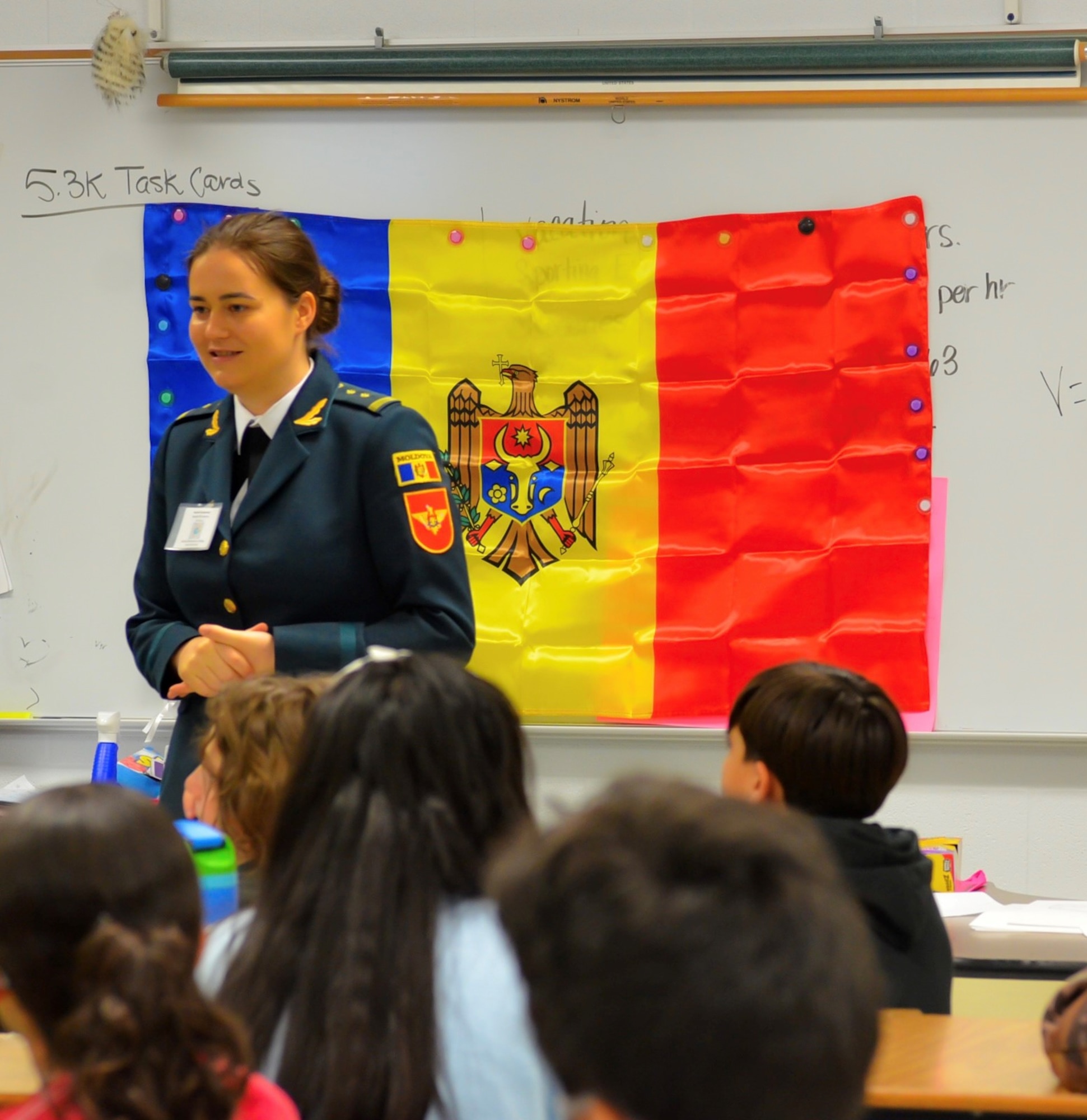 Defense Language Institute English Language Center student talks to elementary students. The Moldovan flag is in the background.