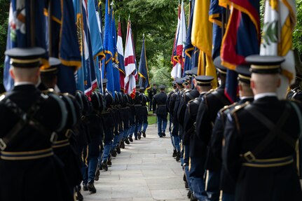Two rows of Army Soldiers dressed in dark ceremonial uniforms are lined up facing away and forming a flag cordon with flags from the U.S. states and territories.