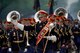 Army Band members dressed in dark uniforms and red hats are marching in formation during a parade while the leader in front is gesturing to the right.