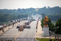 Army Soldiers in various uniforms are seen in the distance marching in serveral formations across a bridge at the start of a parade.