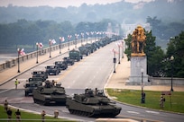 Green tanks and other Army heavy equipment are driving in a line across the Memorial Bridge in Washington, D.C., during a parade.