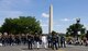 Service members dressed in uniforms from each branch of the military are marching down the street, followed by The U.S. Army Band "Pershing's Own," with the Washington Monument and parade onlookers in the background.
