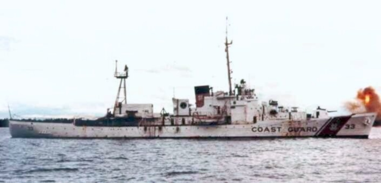 A white ship in the ocean fires shots toward the shore.