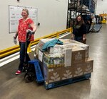 Two people smile while moving a pallet of food.