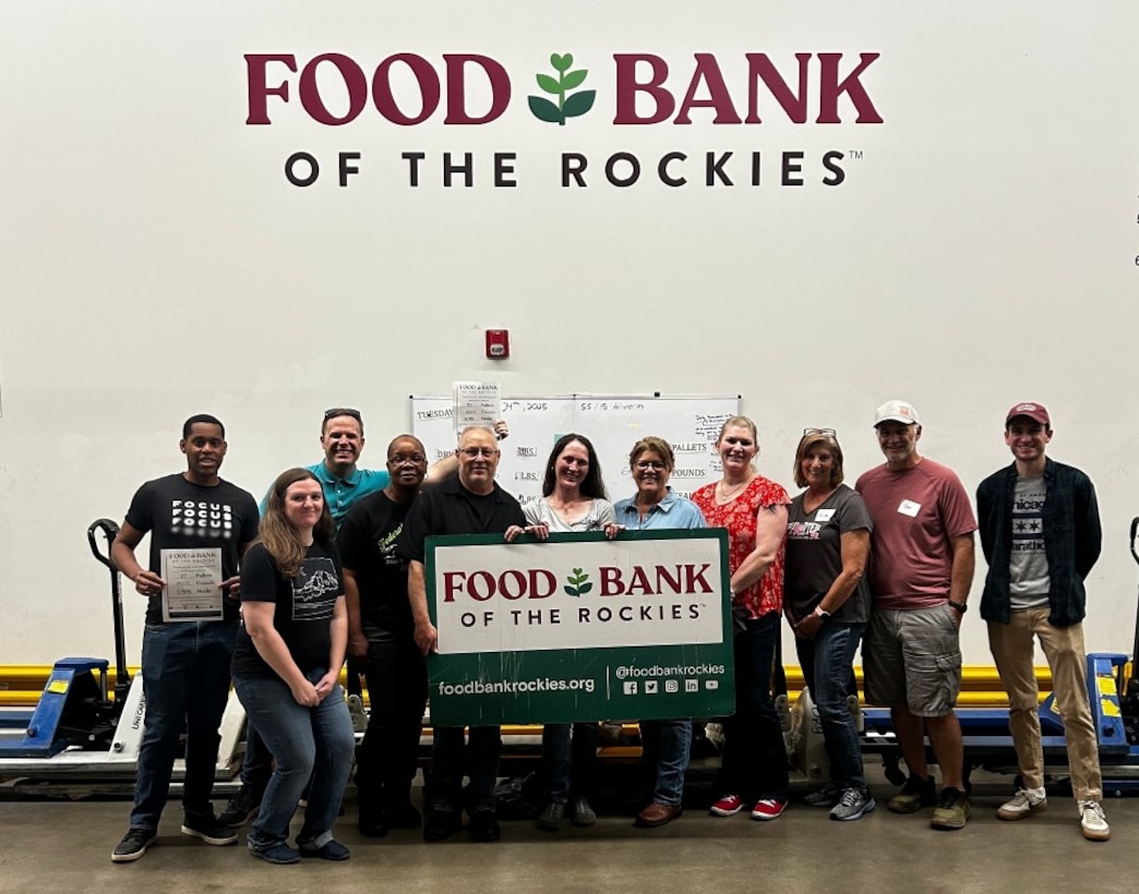 A group of people stand behind a sign of a non-profit they volunteered at.