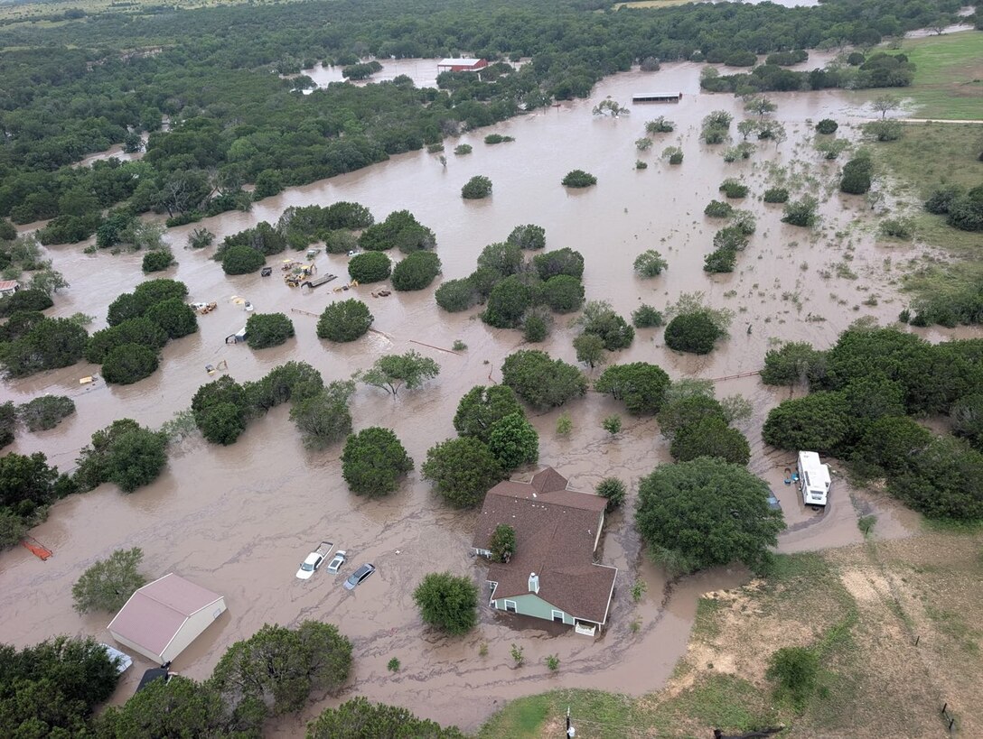 In an aerial shot, homes, trees, streets and cars are submerged in flood water.