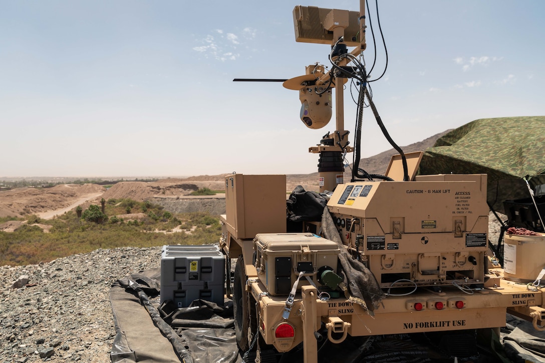 A large, ground-based surveillance system is seen at a rocky area overlooking sparsely vegetated land and small hills.