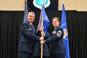Col. Cornelius and Chief Master Sgt. Gilson stand, both holding the guidon.