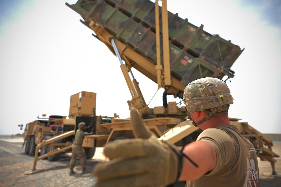 A soldier gives a thumbs up while looking at a Patriot missile defense system.