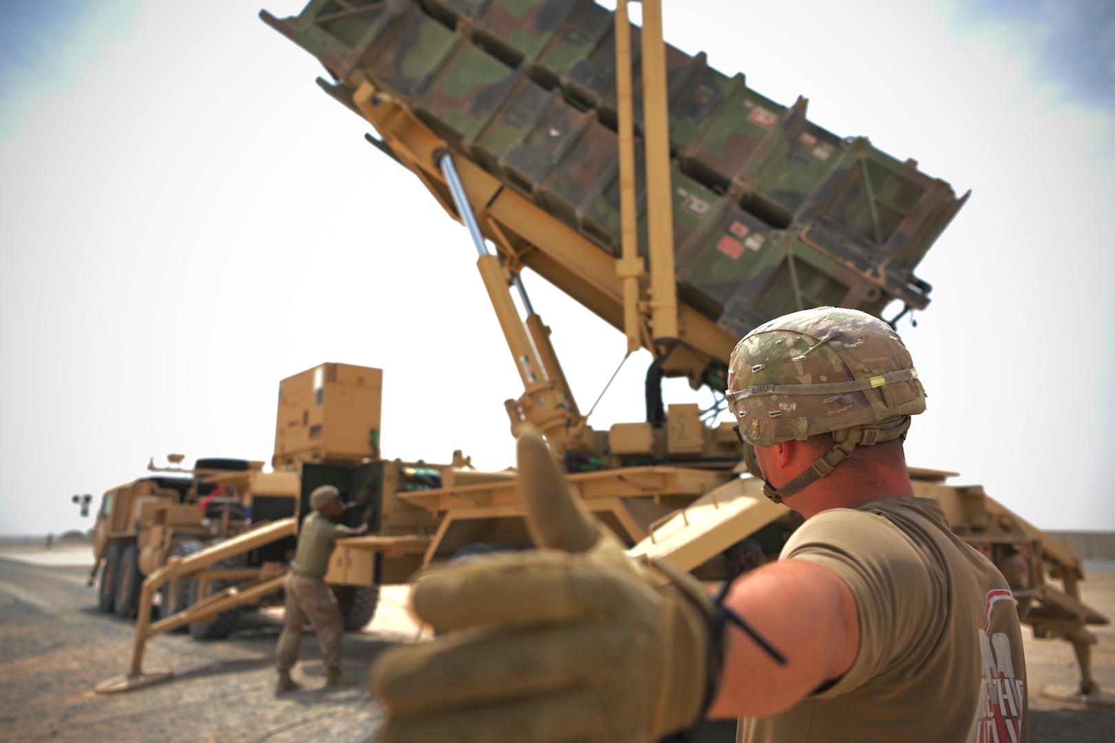 A soldier gives a thumbs up while looking at a Patriot missile defense system.