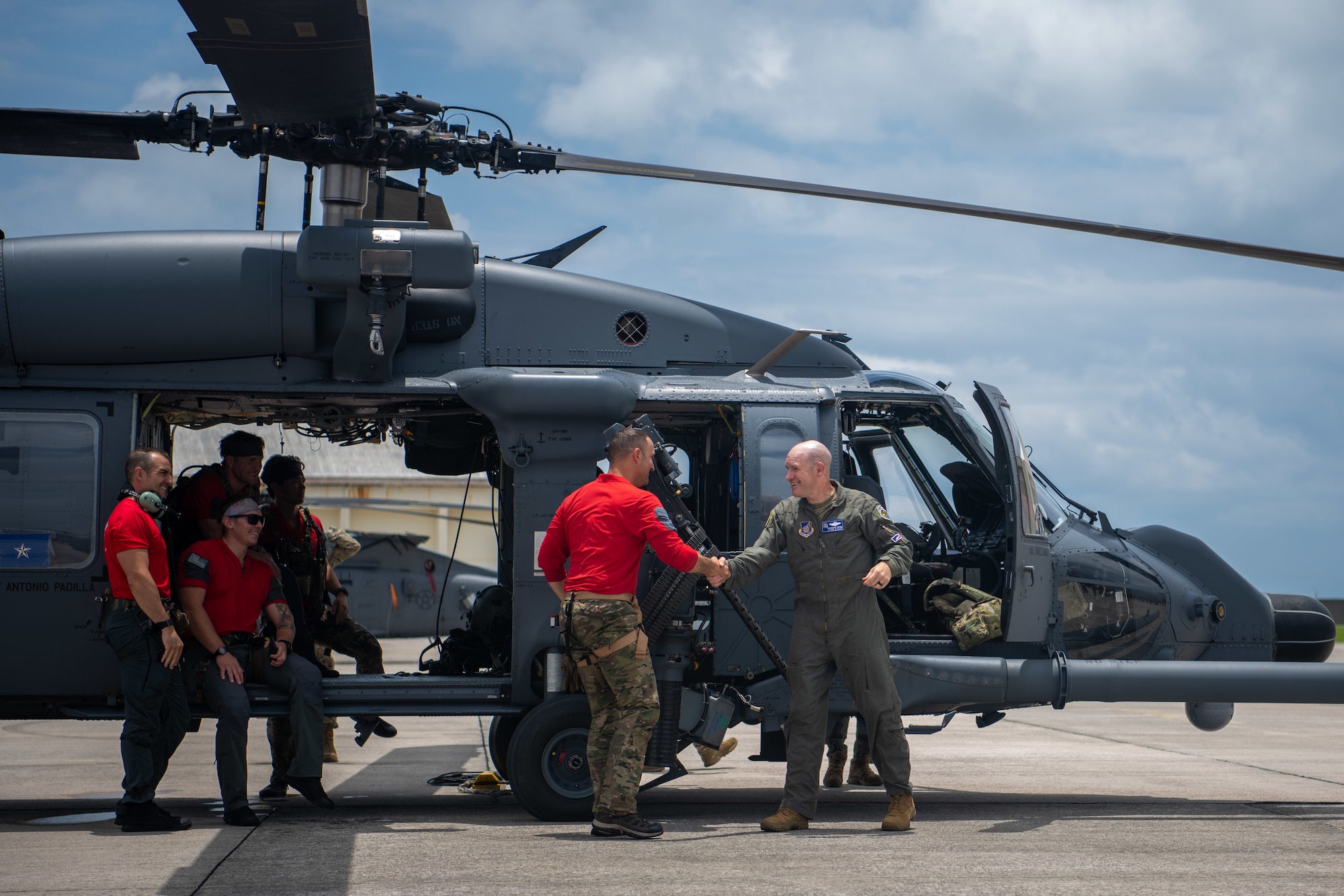 two military members shake hands in front of a HH-60
