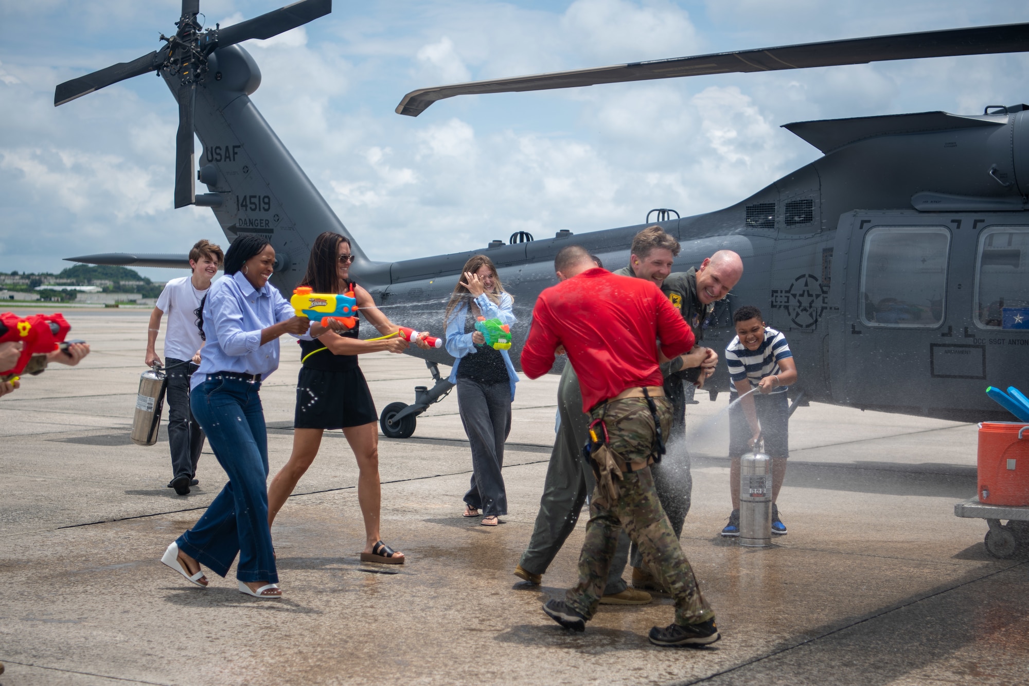 two military members get sprayed with water by their families in front of a HH-60