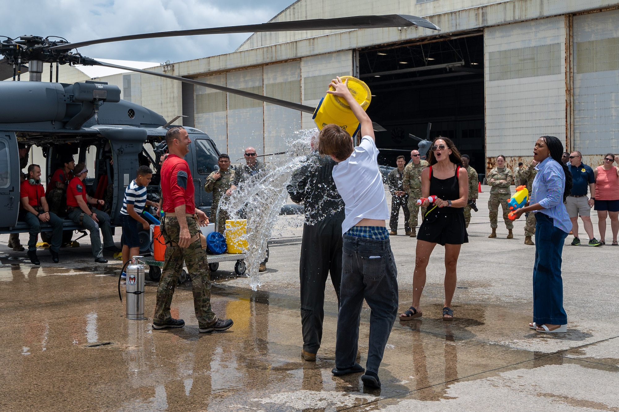 A pilots son pours a gallon of water onto his father next to a helicopter