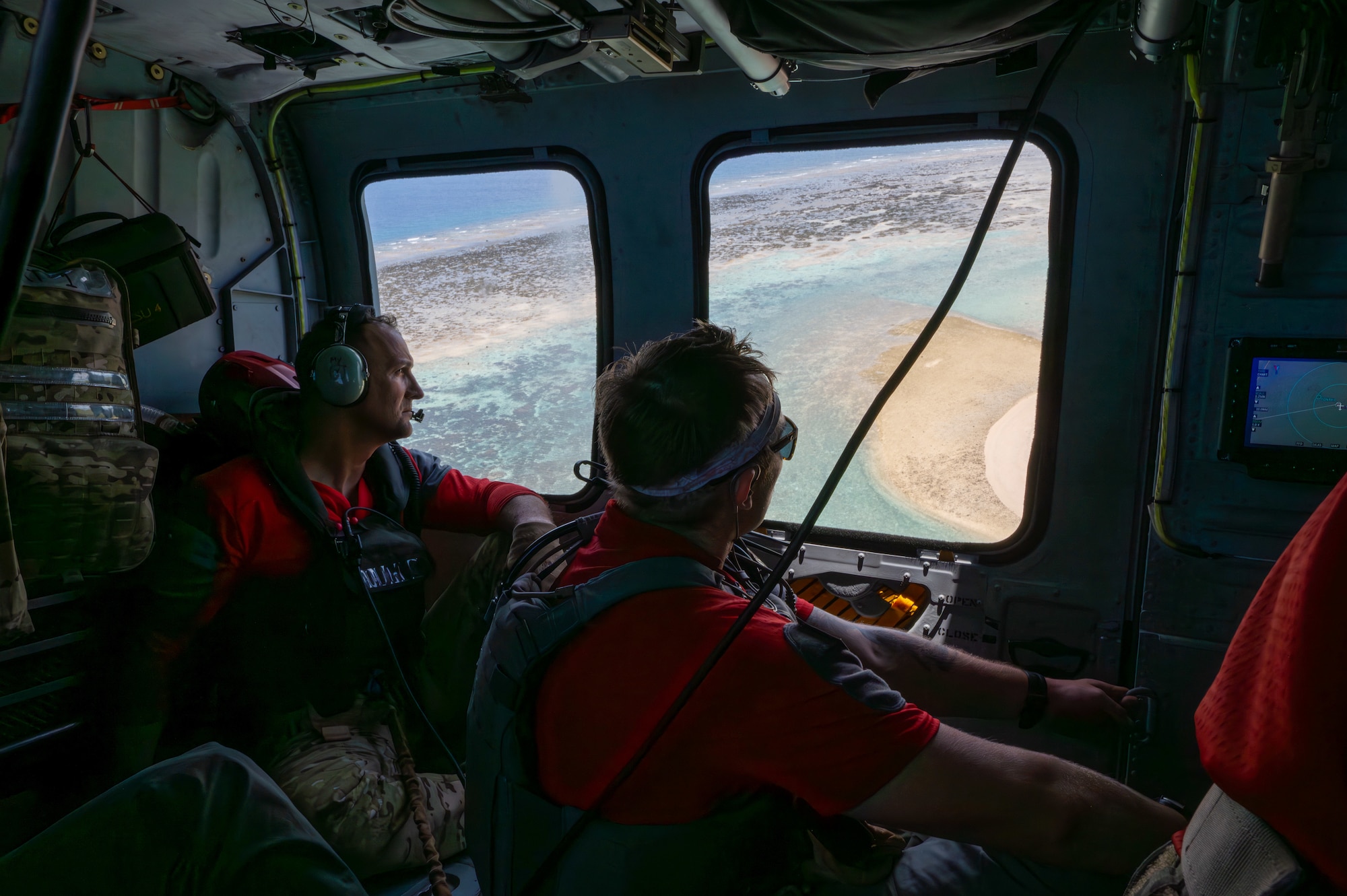 two military members look out of a helicopter window