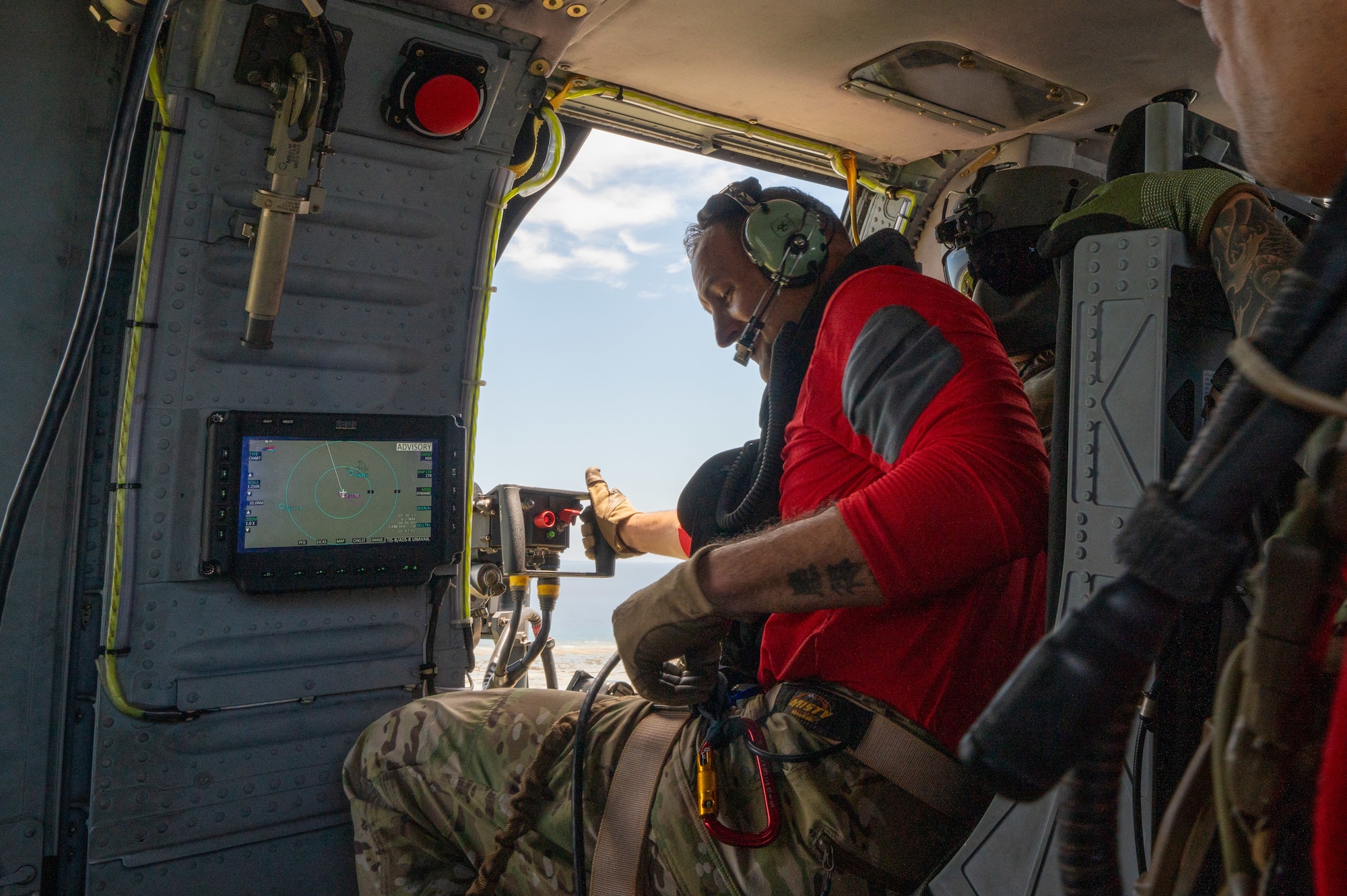 military member sits in the machine gun seat of a HH-60W helicopter