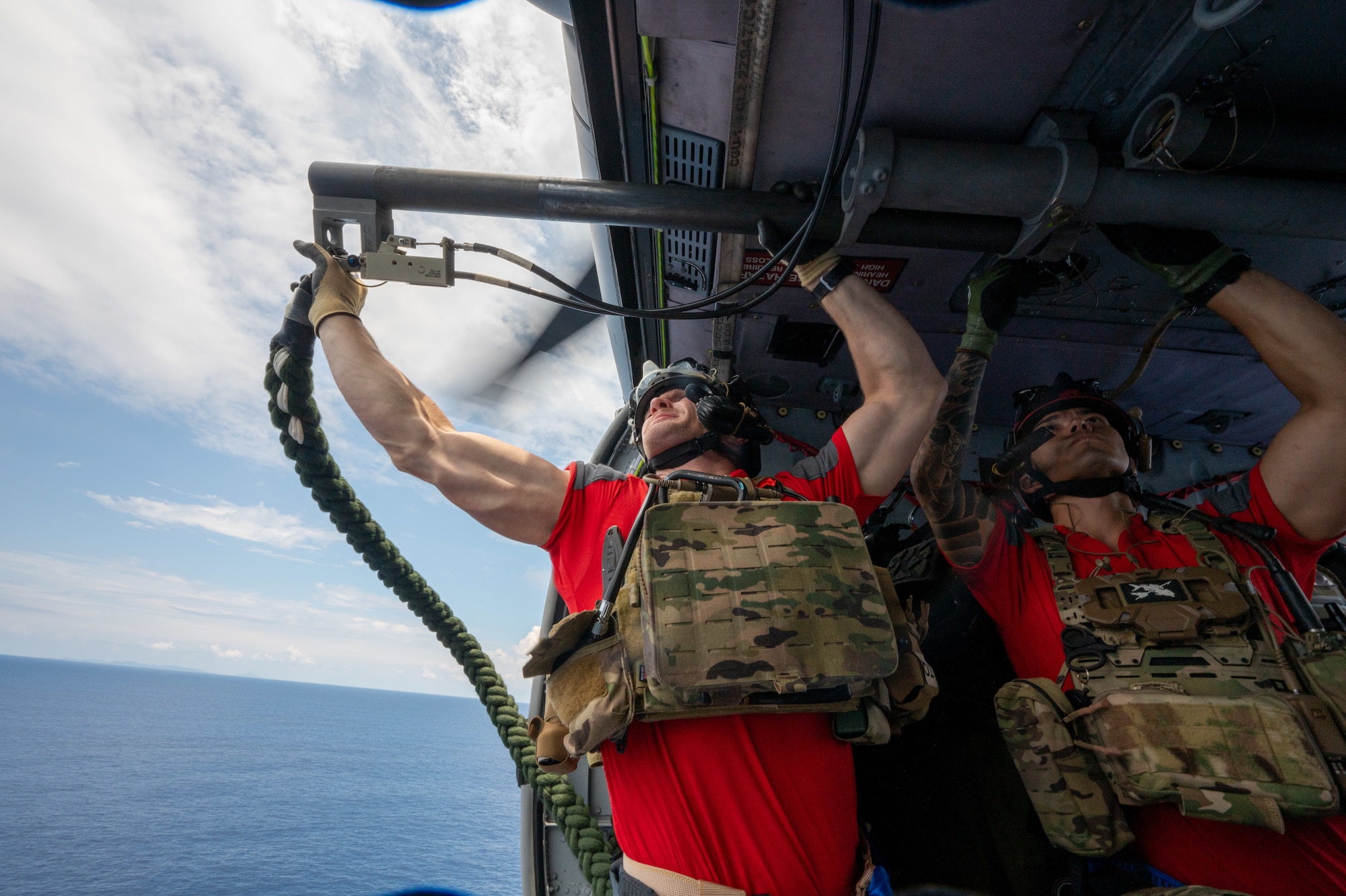 Two military members hold a rope out of a helicopter while inside