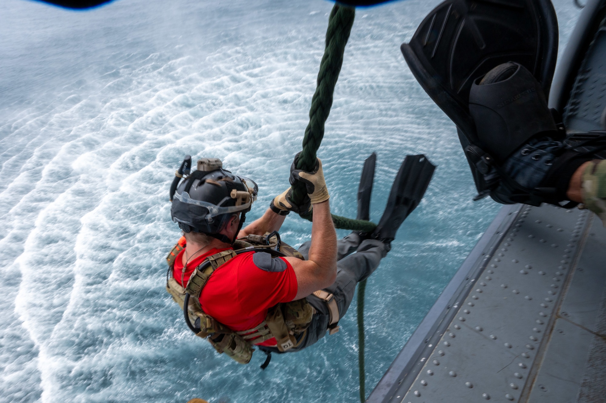 military member sits on a rope as he repels out of a helicopter