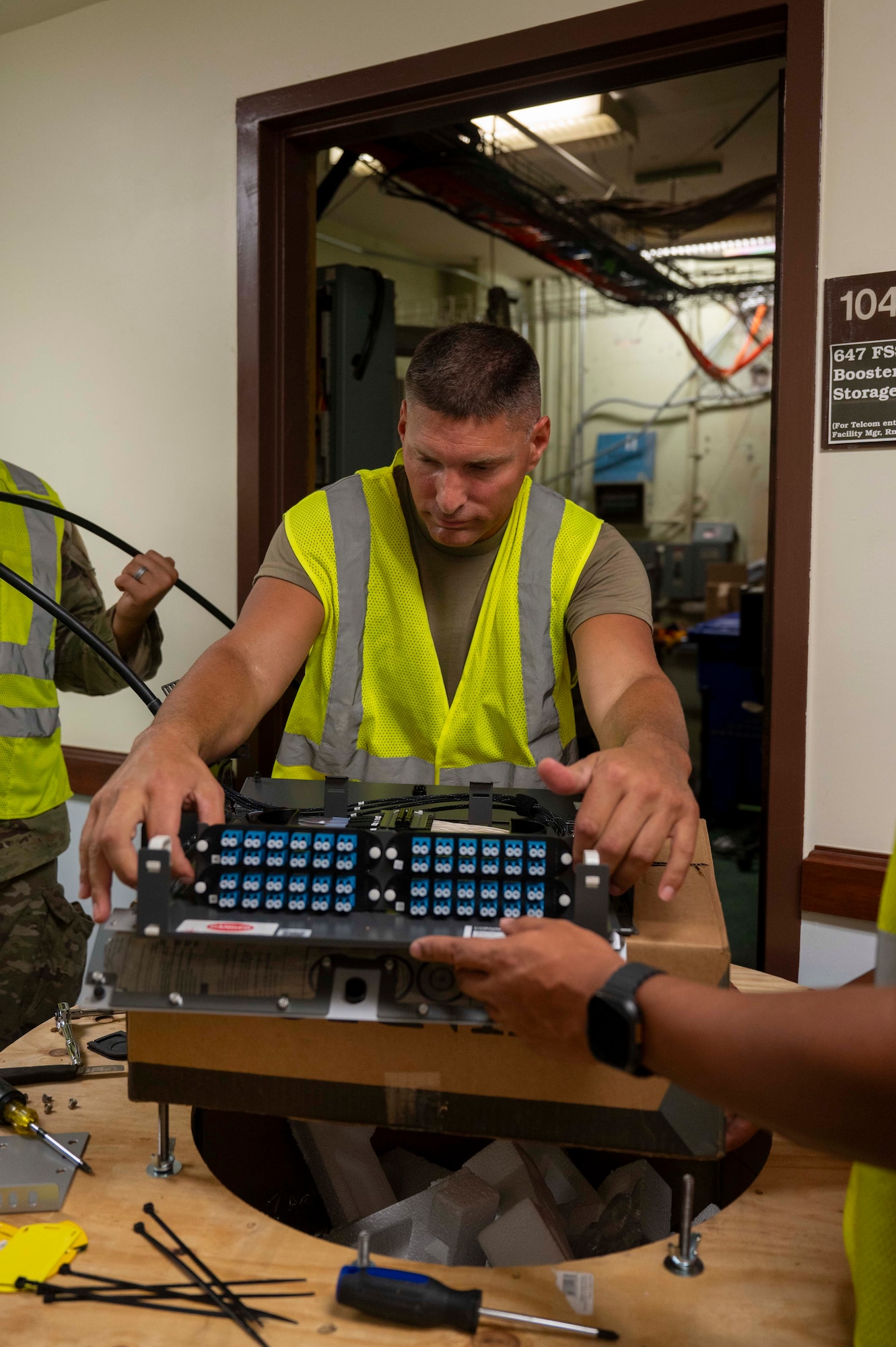 U.S. Air National Guard Staff Sgt. Jonathan Ziemer, 210th Engineering Installation Squadron cable technician, inspects a fiber optic rack-mount connector to be installed in a network cable enclosure at Joint Base Pearl Harbor-Hickam, Hawaii, July 9, 2025. This installation is part of the Fiber Deep project; a strategic initiative designed to enhance base communications and bolster cyber defense capabilities. (U.S. Air Force photo by Senior Airman Melody Bordeaux)