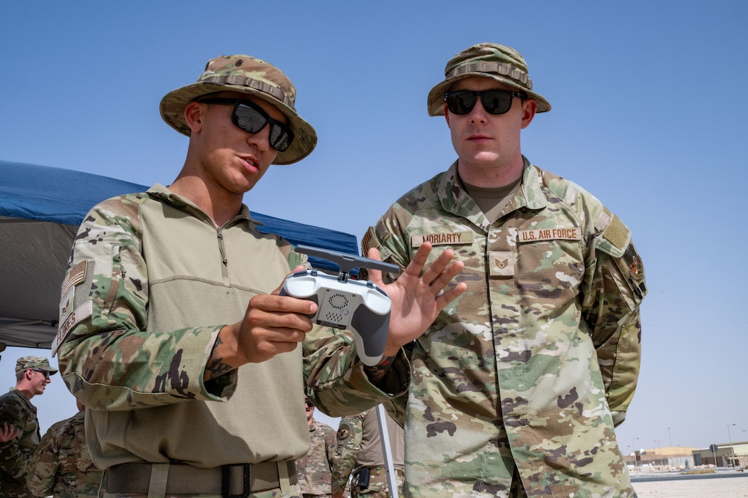 U.S. Senior Airman Nicolas Flores, Task Force 99 small unmanned aircraft systems operator, gives directions to Staff Sgt. Sean Moriarty, 379th Air Expeditionary Wing public affairs specialist, during drone training within the U.S. Central Command area of responsibility, May 26, 2025. TF-99 is an innovation cell that tests and refines new technologies, ensuring that they can respond to pacing threats with advanced operational solutions. (U.S. Air Force photo by Senior Airman Amanda Jett)