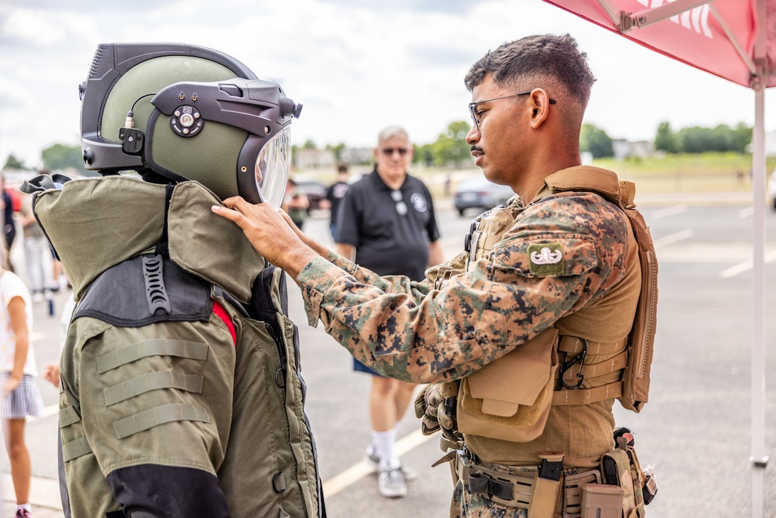 U.S. Marine Corps SSgt. Jalen Riddle, an explosive ordnance disposal (EOD) technician with 8th Engineer Support Battalion, shows a member of the community an EOD suit at Romeoville High School during Marine Week Chicago, July 10, 2025. During Marine Week Chicago, Marines with Marine Corps Recruiting Command shared Marine Corps traditions with local high schools in honor of the Corps’ 250th birthday. The Marine Corps is celebrating its 250th birthday with six multi-day Marine Corps community events, called Marine Weeks, in six major cities across the country. Marine Weeks will include activations across each host city featuring aircraft, equipment, recruiting opportunities, and public engagements. (U.S. Marine Corps photo by Staff Sgt. Brandon Salas)