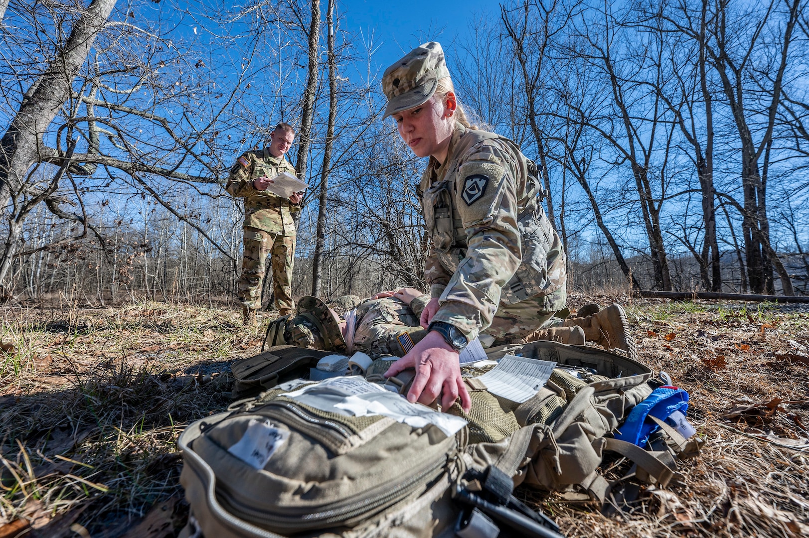 a soldier works a fellow soldier outside in the winter woods, as the second soldier is role-playing as injured with mock medical injury make-up on