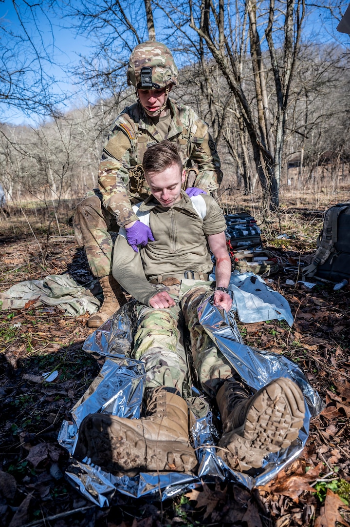 a soldier drags a fellow soldier outside in the winter woods, as the second soldier is role-playing as injured with mock medical injury make-up on