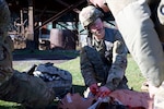 a soldier works on a "bloodied" medical dummy outside