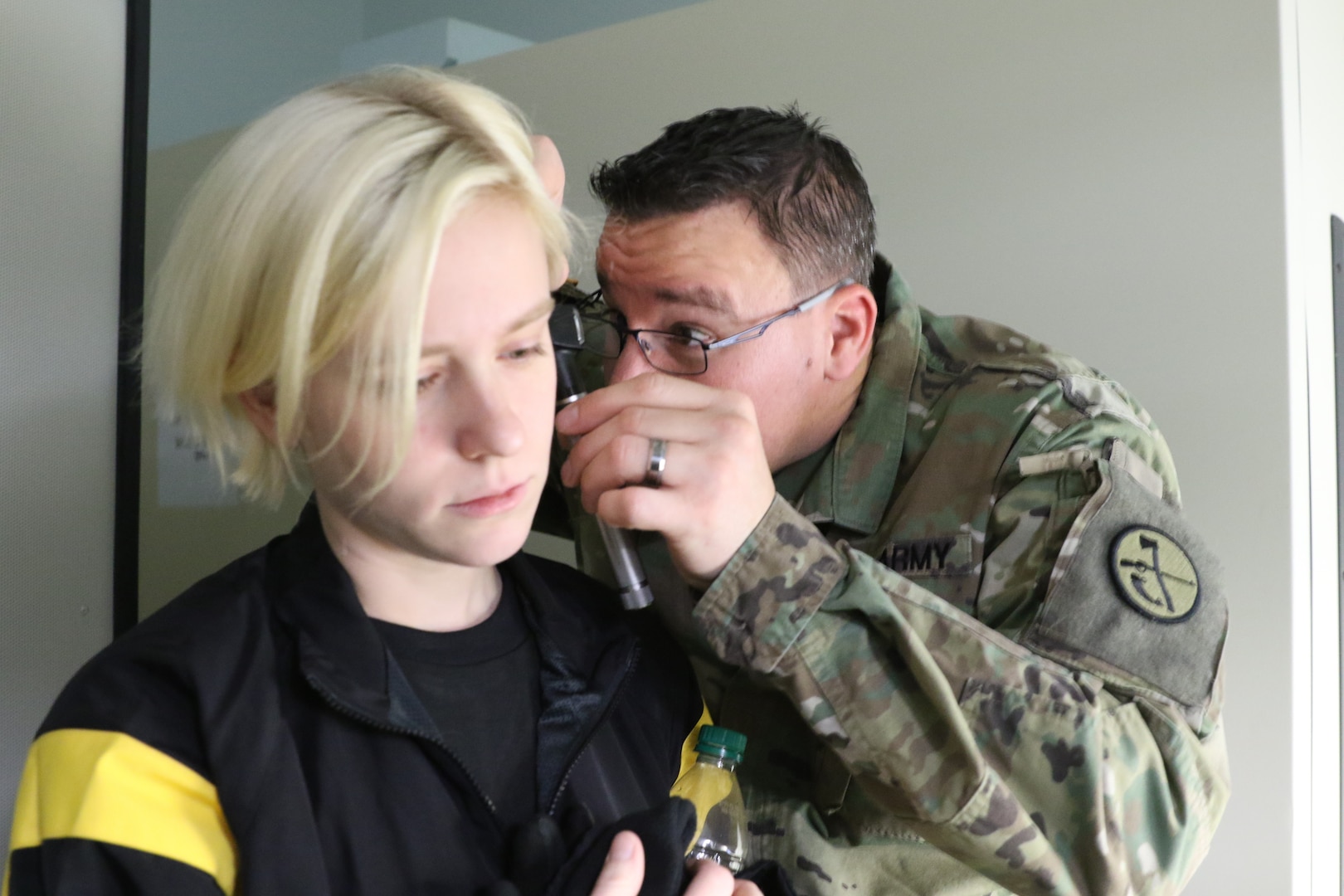 A blond soldier gets an ear exam by a soldier in camo uniform