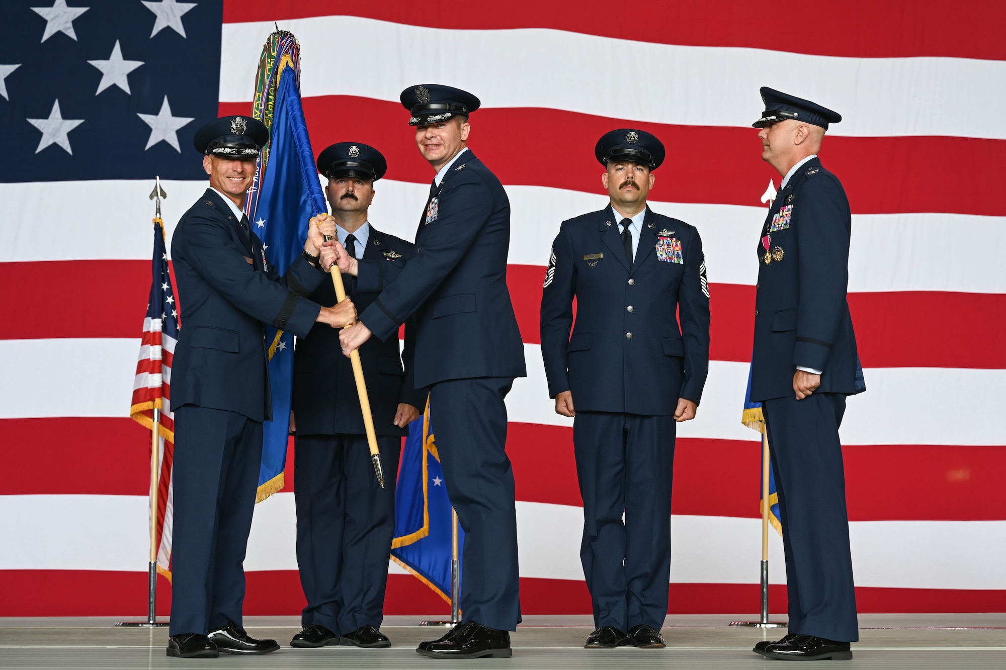 U.S. Air Force Maj. Gen. Gregory Kreuder, 19th Air Force commander, passes the 97th Air Mobility Wing (AMW) guidon to Col. Richard Kind, 97th AMW commander, during the wing change of command ceremony at Altus Air Force Base, Oklahoma, July 11, 2025. Kind served as the deputy commander of the 375th Air Mobility Wing prior to taking command at Altus. (U.S. Air Force photo by Airman 1st Class Lauren Torres)