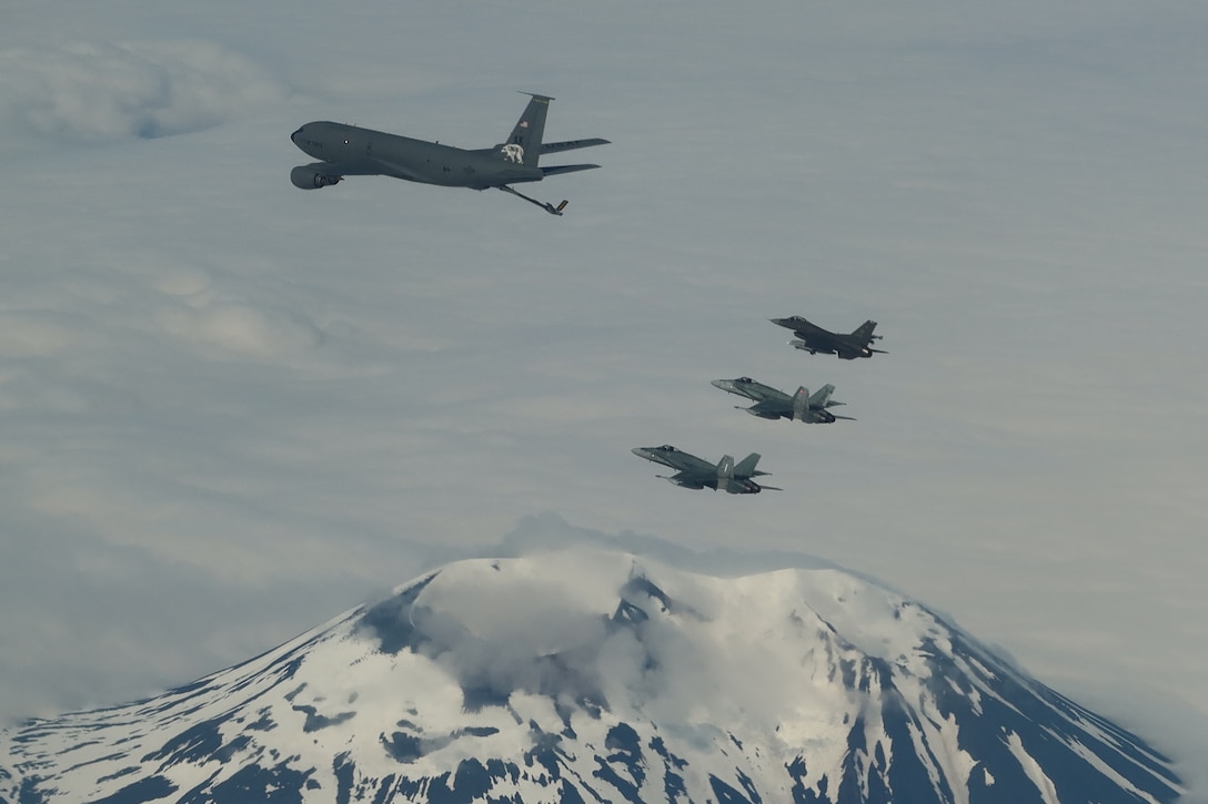 One large aircraft flies near three smaller aircraft with a snowy mountain behind.