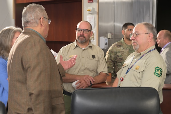 Four people are in a discussion in a conference room, with two of the people facing the camera wearing U.S. Forest Service uniforms