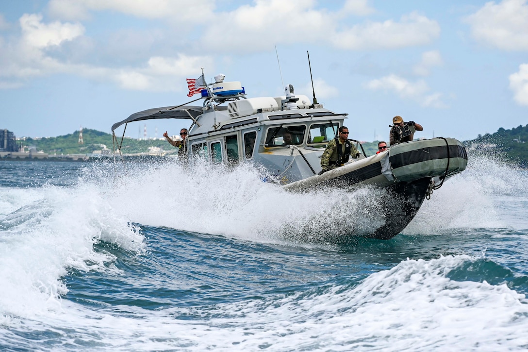Sailors look out from a boat as it sails through waves under partly cloudy skies.