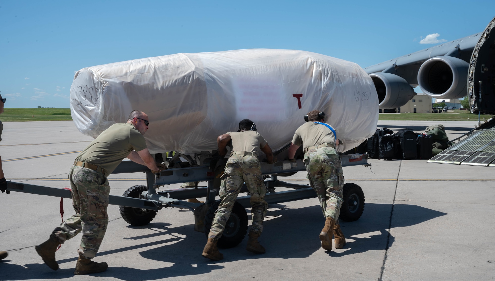 Airmen from the 5th Logistics Readiness Squadron (5LRS) help push a B-52H Stratofortress engine into place to be put onto a C-5M Super Galaxy at Minot Air Force Base, North Dakota, July 1, 2025. The 5LRS air transportation function at Minot AFB plays a critical role in ensuring mission success by loading and moving essential cargo to support global operations. (U.S. Air Force photo by Airman 1st Class Wesley Davies)