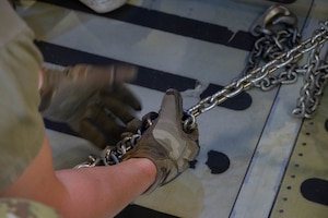 An Airman from the 5th Logistics Readiness Squadron tightens a chain holding cargo in place in a C-5M Super Galaxy at Minot Air Force Base, North Dakota, July 1, 2025. Airmen from the 22nd Airlift Squadron at Travis Air Force Base work with Minot AFB to help facilitate global deterrence and provide vital supplies to Minot Airmen on missions. (U.S. Air Force photo by Airman 1st Class Wesley Davies)