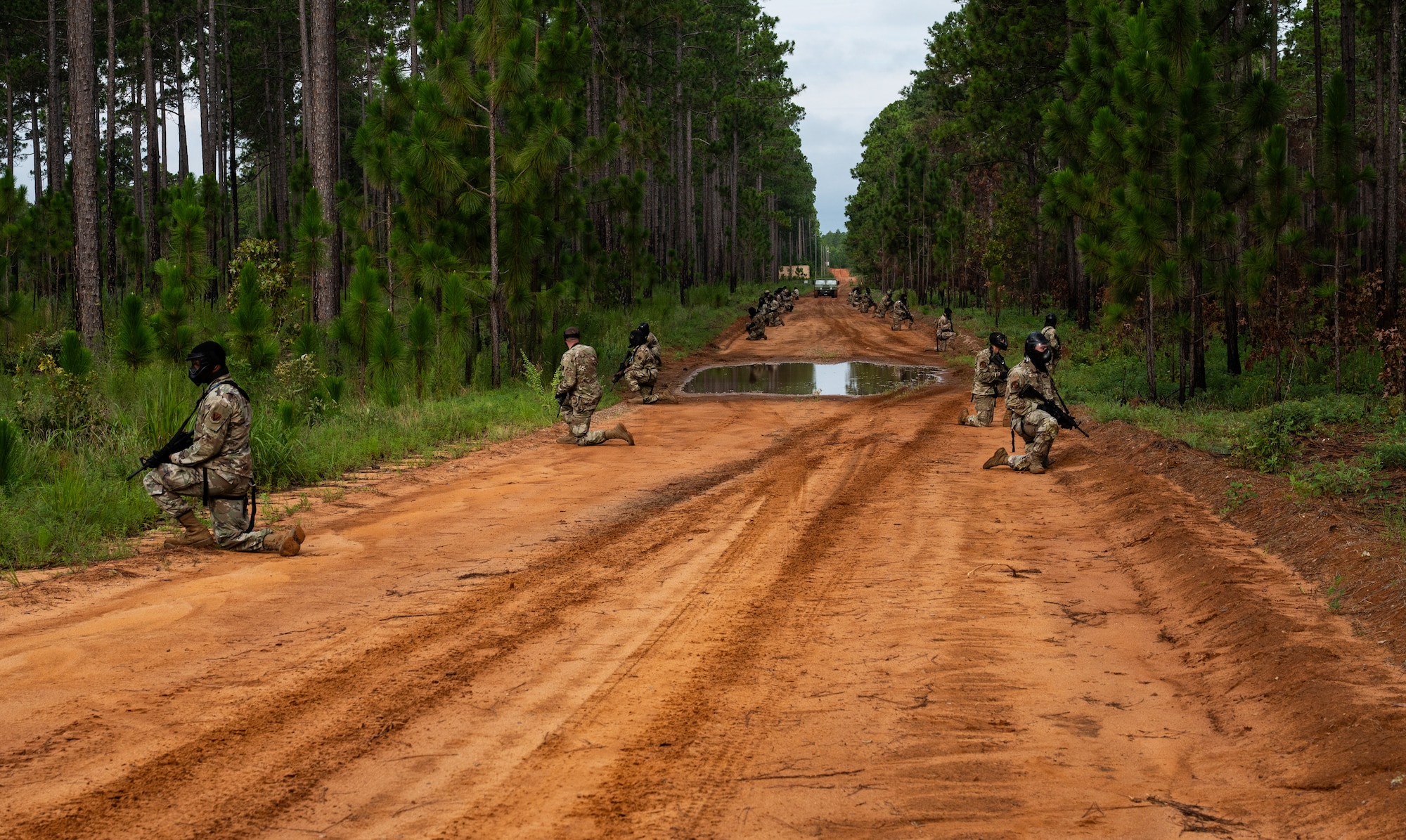 Airmen line up across the sides of a dirt, holding weapons and wearing tactical face masks.