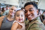 Woman, baby, and service member smile and pose together