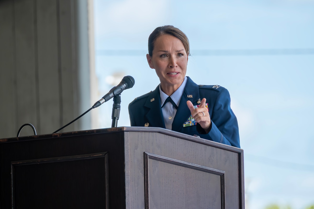 A female colonel stands behind a podium and speaks.